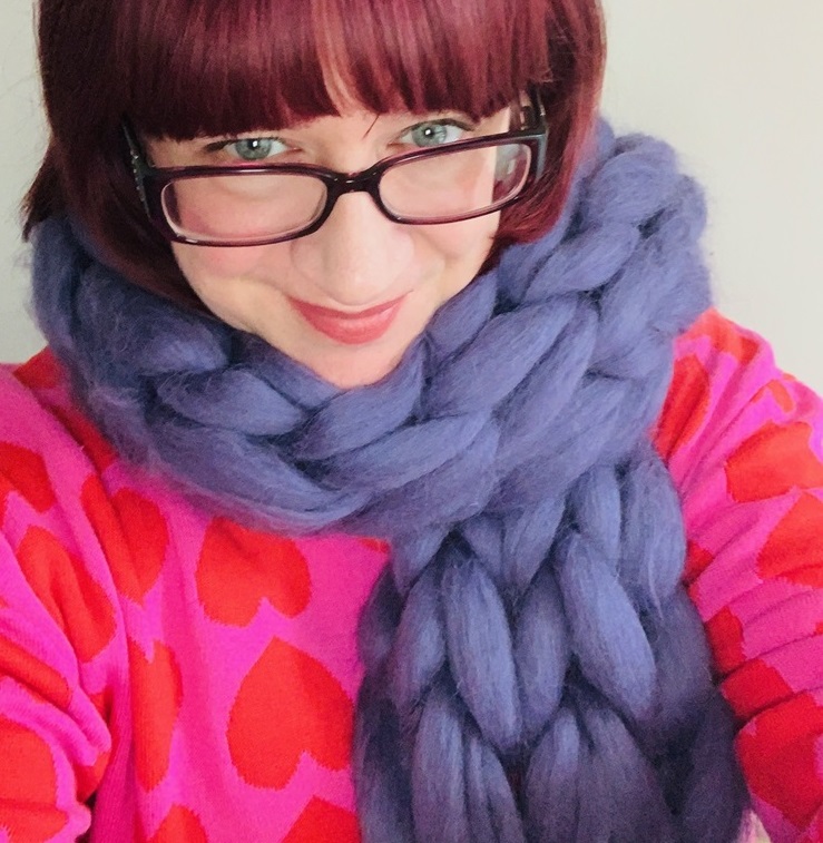 Woman wearing arm knitting chunky purple scarf.