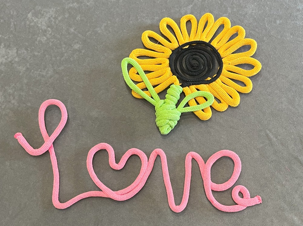 Two yarn covered wire shapes. One says "Love" in pink yarn with a heart in the middles. One is a sunflower made from yellow yarn loops with brown middle and green shaped into leaves.