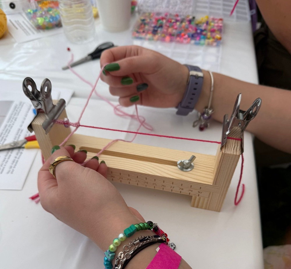 Close up of hands making a friendship bracelet on a jewellery clamp at a bracelet making workshop. Pots of beads in background.