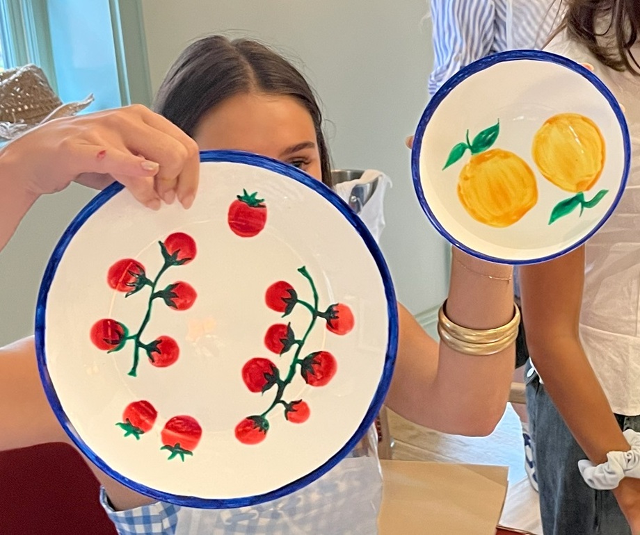 Woman holding painted plates featuring fruit designs.