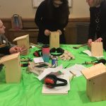 Table set for bird box making workshop, set with green table cover, finished bird boxes, instruction packs, hammers and ear defenders.