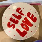 Painted plate featuring the slogan "Self Love" in red bubble writing, painted at a corporate pottery painting workshop