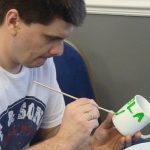 Painting a mug with green letters during a corporate mug painting workshop