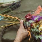 Hands wiring dried flowers to a straw wreath ring in dried wreath making workshop.