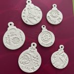 Finished white clay Christmas decorations in bauble designs, embossed with Christmas shapes and patterns.