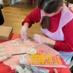 Christmas clay workshop in progress - woman wearing apron, making Christmas clay decorations. Table set with rolling pin, stamps, cookie cutters and letter press kit.