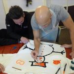 Christmas jumper painting workshop in progress - two men painting a white jumper with snowman design.