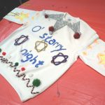 Hand painted Christmas jumper on red table, with "o Starry Night" design decorated with tinsel pompoms and pipe cleaners.