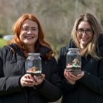 Two women outside wearing winter coats each holding a small terrarium.