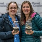 Two women wearing winter coats each holding a small terrarium.