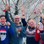 Team holding the baubles they just made in bauble decorating workshop in front of snow-covered trees.