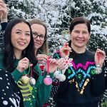 Team holding the baubles they just made in bauble decorating workshop in front of snow-covered trees.
