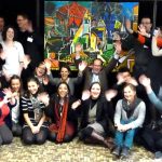 Team posing in front of giant painting painted in painting team building activity.