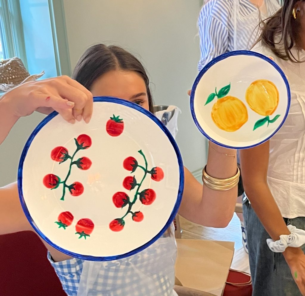 Holding a painted plate and bowl featuring fruit designs, painted at a corporate pottery painting workshop.