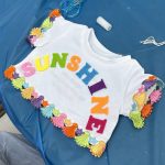 Teddy bear T shirt that says "Sunshine" in bright colours, made in charity team building activity.