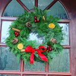 Traditional fresh Christmas wreath made with green foliage, pine cones, oranges, cinnamon red baubles and red bow, hanging on door.