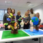 Team standing behind table of sculptures in corporate team sculpting activity.
