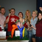 Team celebrating behind table of sculptures at corporate team sculpting activity.