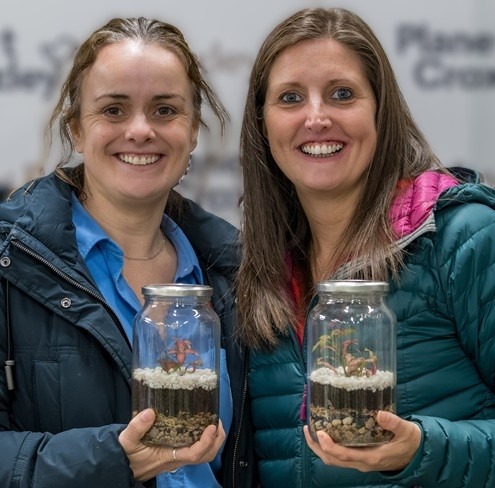 Two women holding small terrariums.
