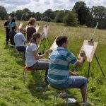 Team of people painting at easels outside, taking part in a corporate watercolour art class.